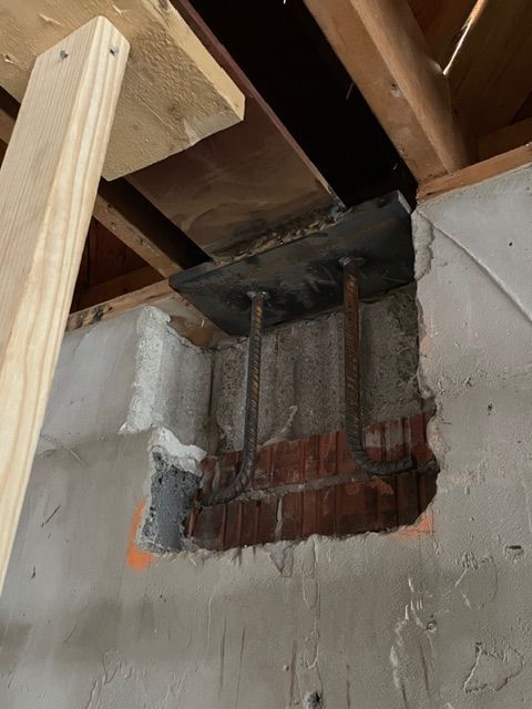 Opening in wall revealing steel beam supports and brick. Wood bracing in the upper left.