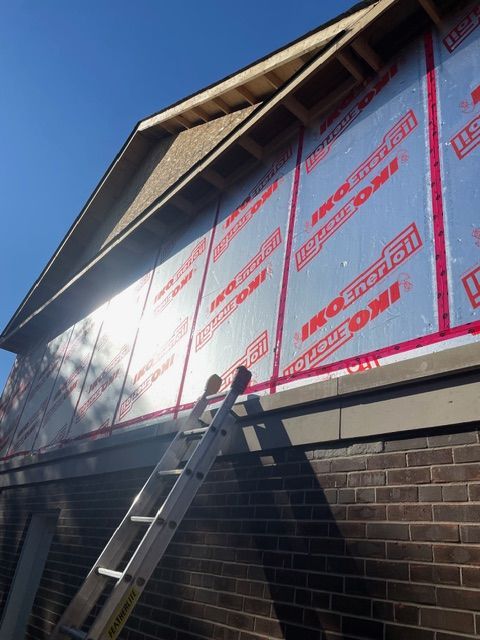 Exterior view of a building under construction, with reflective insulation and a ladder.