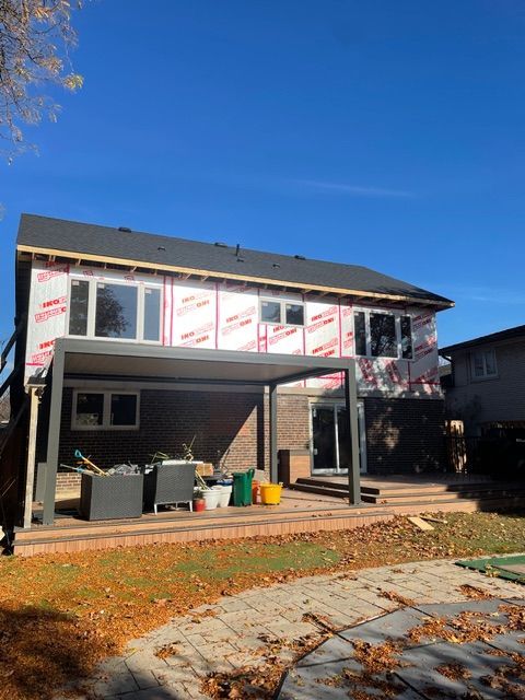 Rear view of a two-story house under construction. Pink insulation exposed, new windows, and a patio with a pergola.