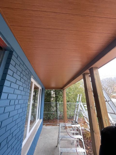 Brown wooden ceiling installed on a porch. Blue brick wall on the left, wooden support columns on the right.