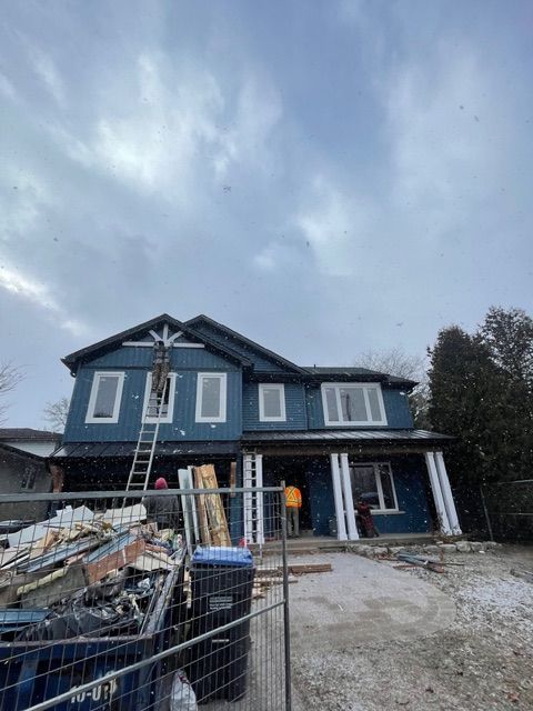 House under construction with blue siding, white trim, and a cloudy sky.