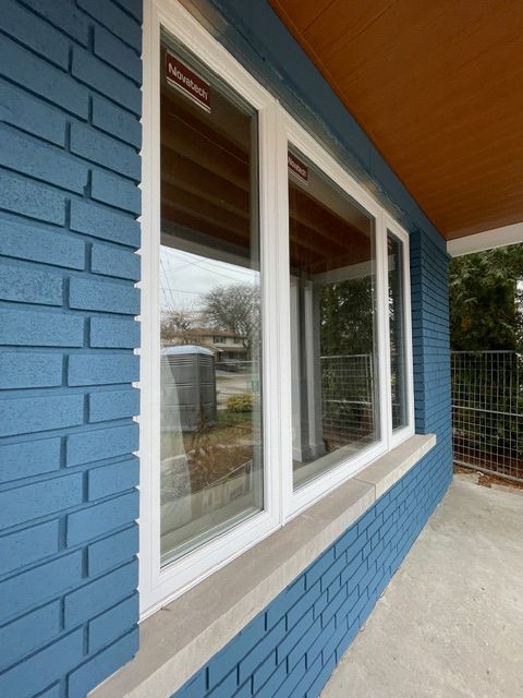 Blue brick exterior with white-framed windows reflecting surroundings. Concrete ledge below windows.