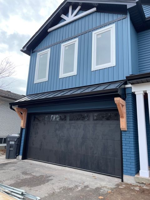Two-story blue house with a black garage door and brown wooden supports.