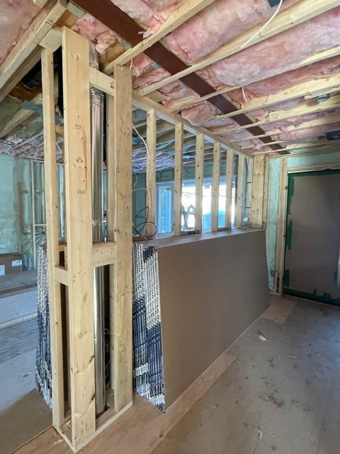 Interior view of a room under renovation. Wooden framing and drywall are visible with insulation and an unfinished ceiling.