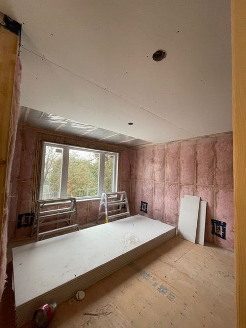 Room under construction with pink insulation, drywall, and a window.