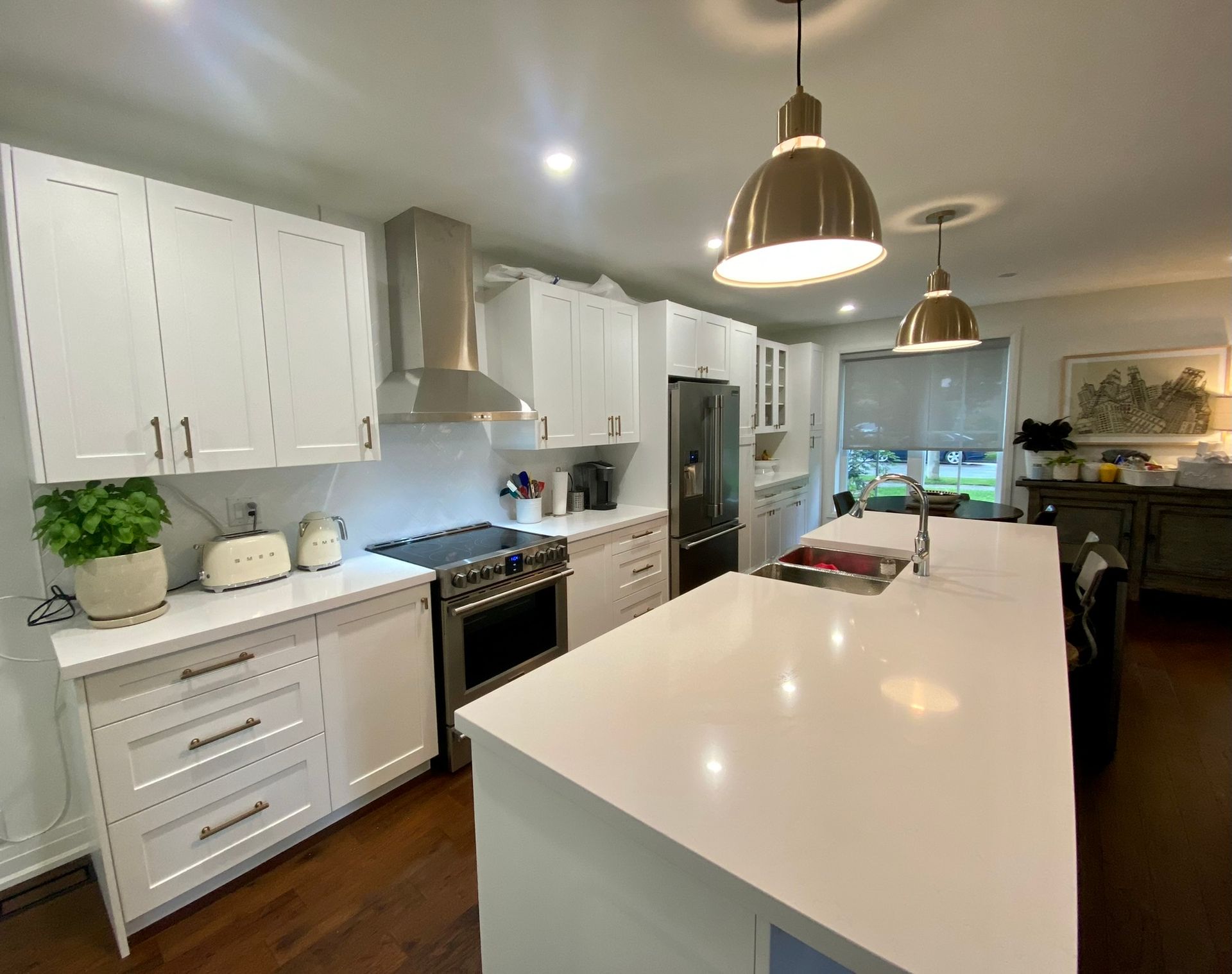 White kitchen with island, stainless steel appliances, and gold pendant lights.