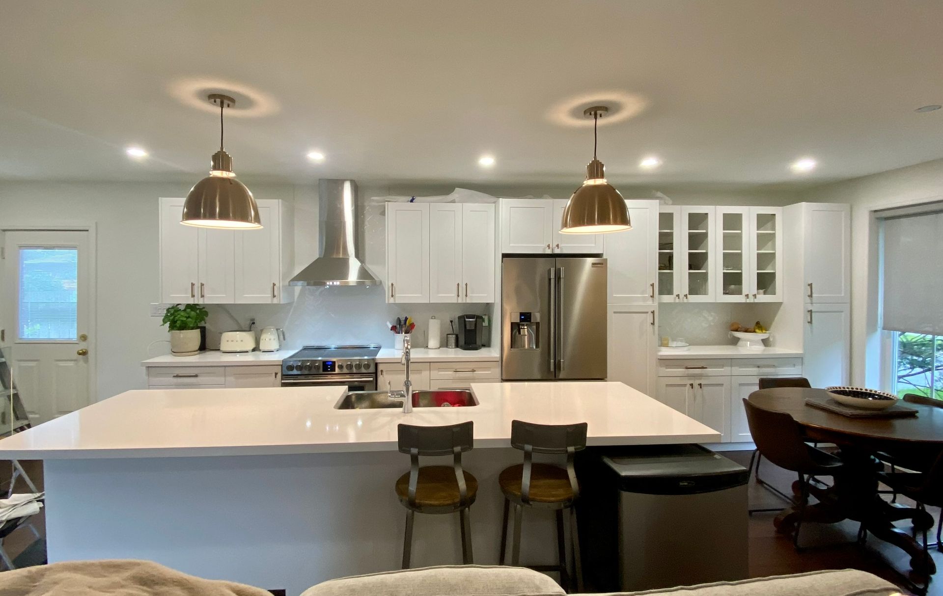 Modern white kitchen with island, stainless steel appliances, and pendant lights.