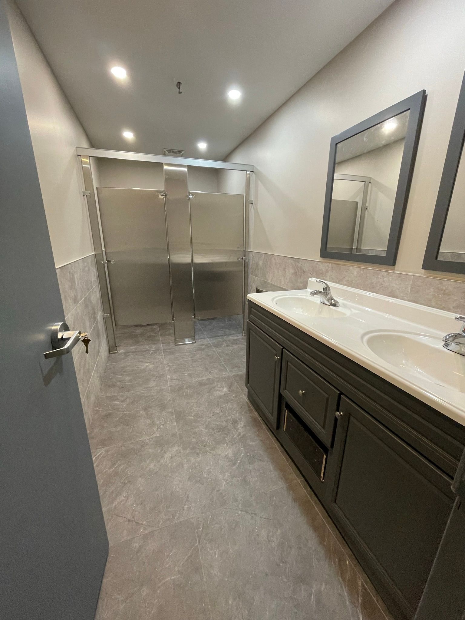 Bathroom with shower, double sink vanity, mirrors, and gray walls and floor.