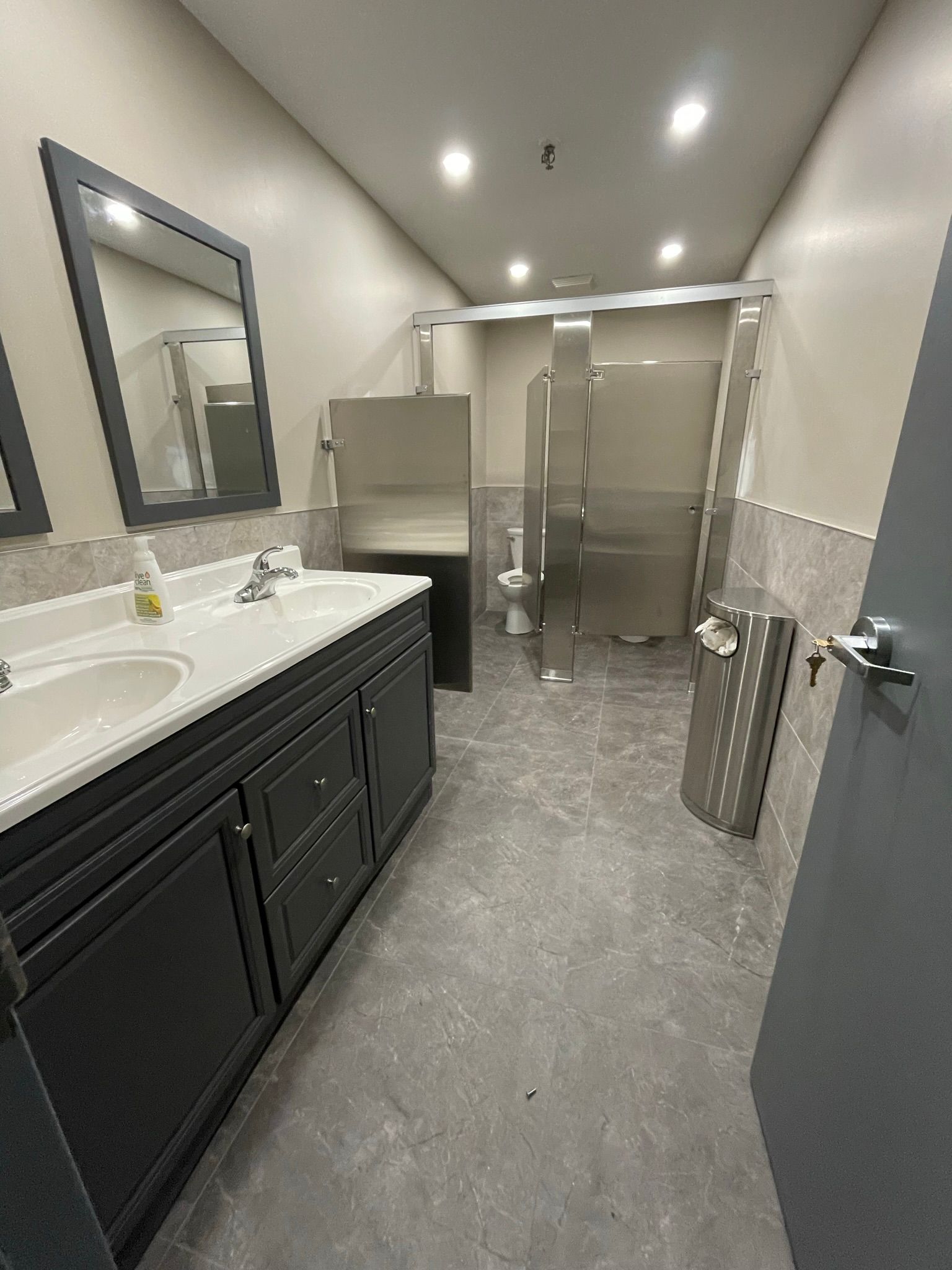 Public restroom with dark vanity, silver stalls, and gray flooring.