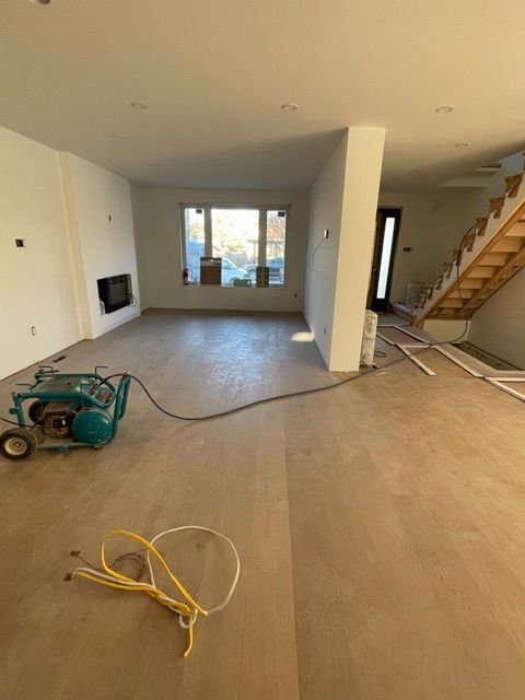 Interior of a room under construction with new wooden flooring and a fireplace. A machine and electrical wires are visible.