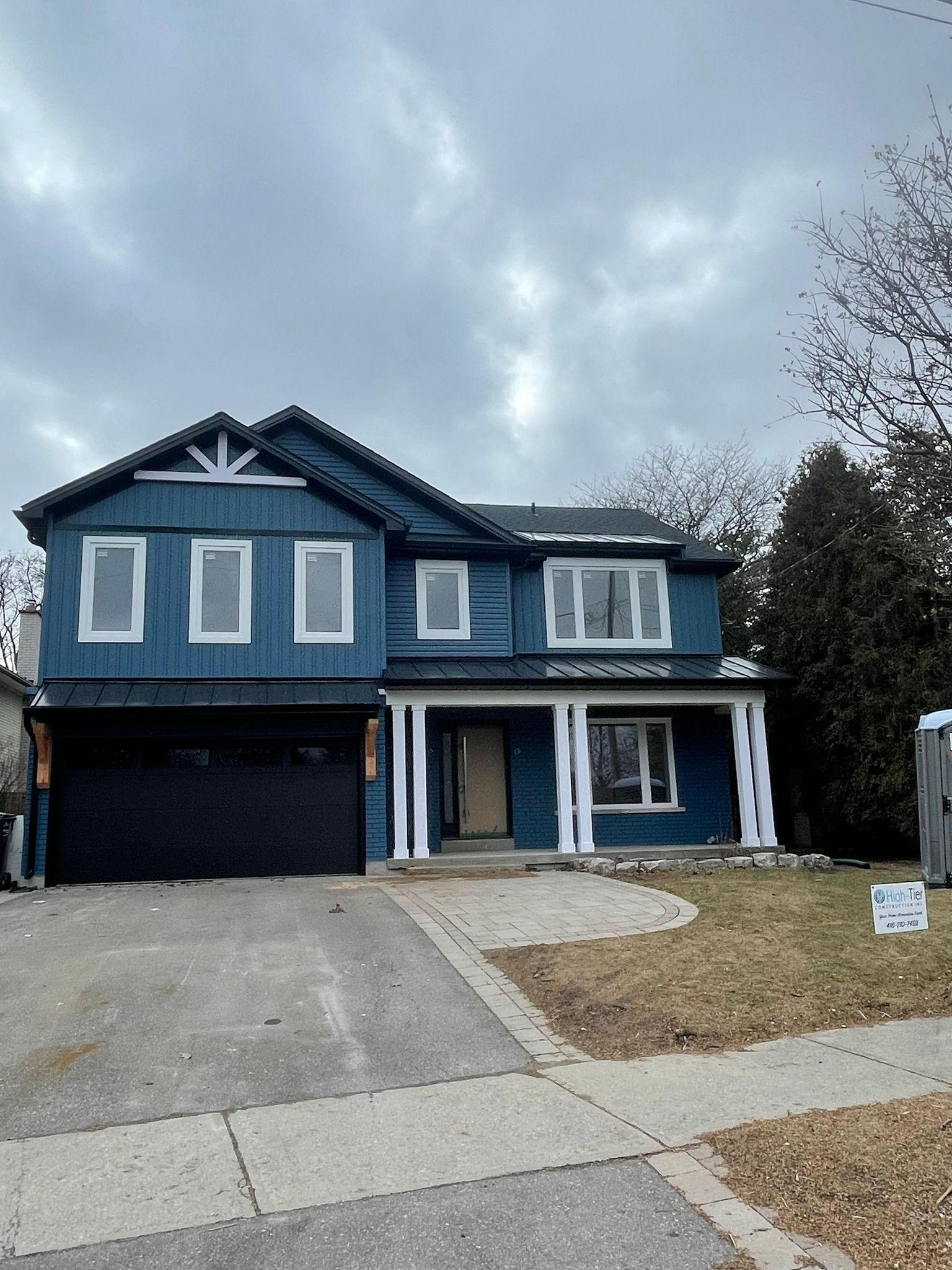 A large blue house with a black garage door is for sale.