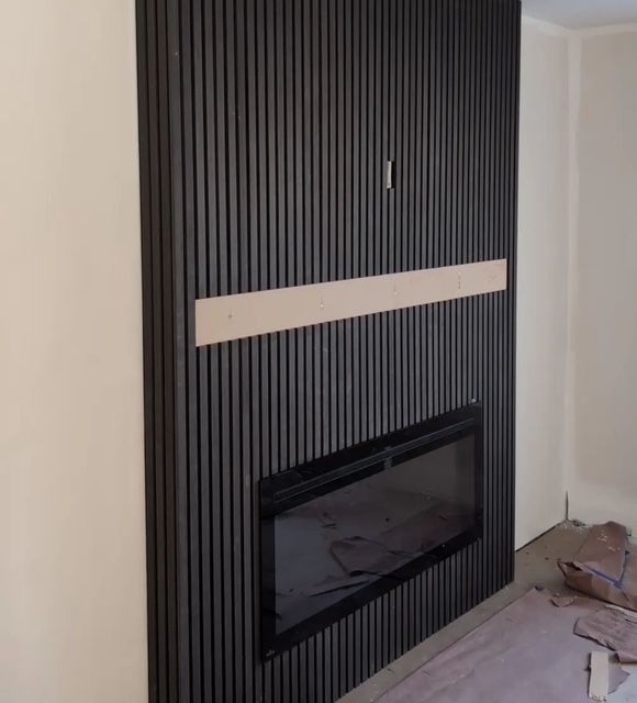 Black vertical slatted wall with built-in fireplace. Unfinished wood trim. Beige walls.