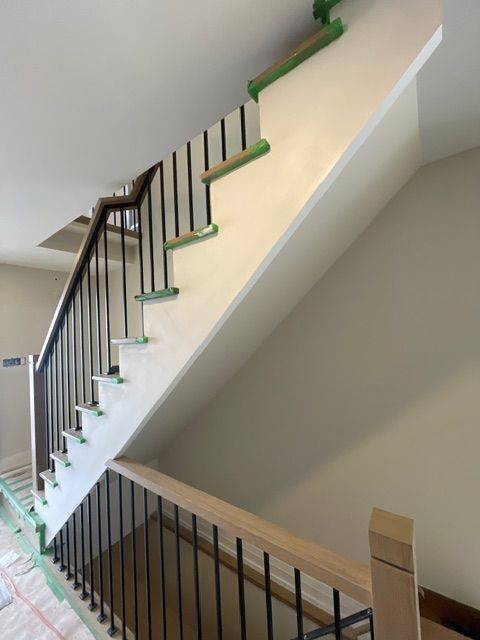 Staircase with black metal railings, wooden handrails, and white and beige walls. Green tape protects some surfaces.