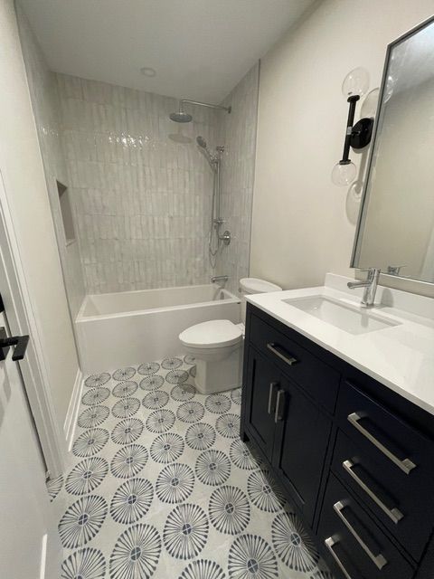 Bathroom with white tub, toilet, and vanity with blue cabinets. Patterned floor.