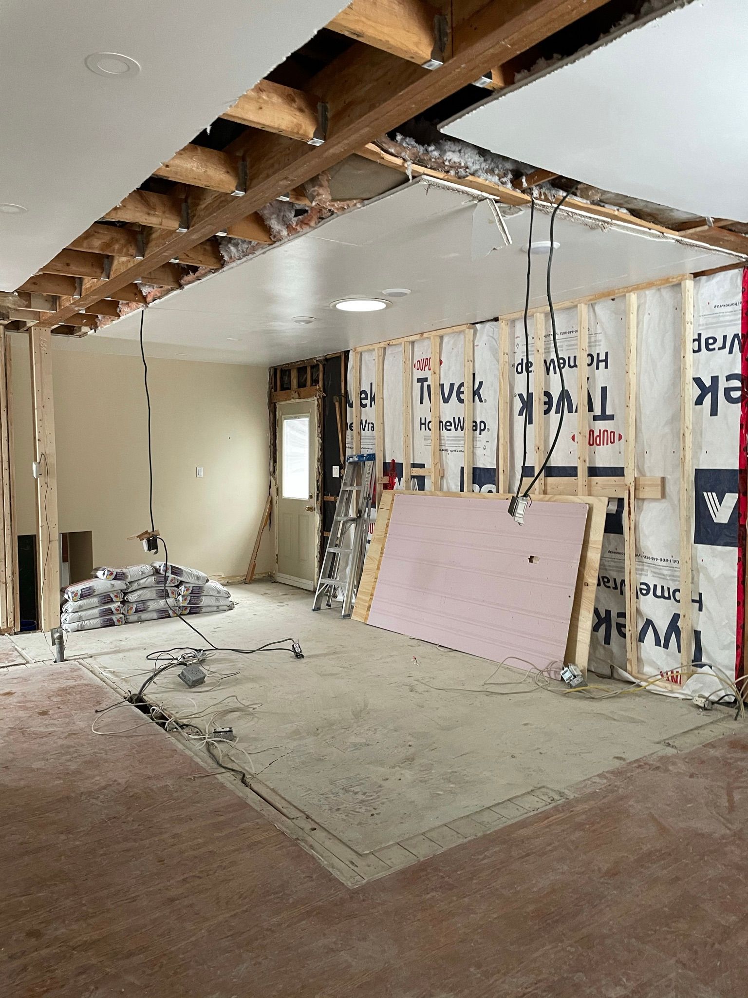 Interior of a room under construction, with exposed beams, drywall, wiring, and insulation visible.