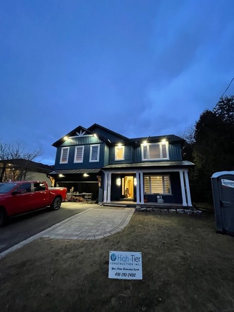 Blue house with bright lights at dusk, red truck parked on the left, and a portable toilet on the right.