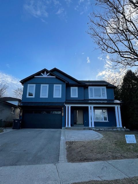 Two-story blue house with white trim. Garage door on the left, front door under covered porch. Cloudy sky.