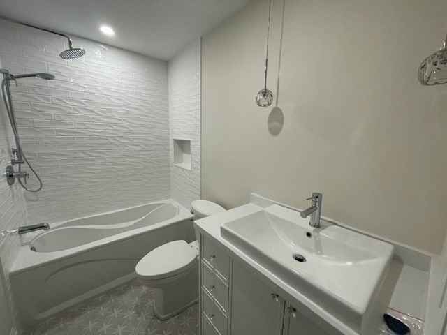 Modern white bathroom with tub, toilet, and sink. Textured shower wall.