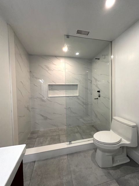 Modern bathroom with marble-tiled shower, glass door, built-in shelf, and a white toilet.