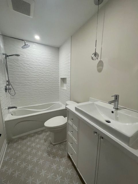 Modern white bathroom with tub, toilet, vanity, patterned floor, and hanging lights.