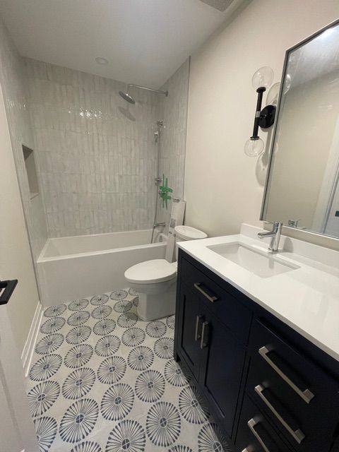 Bathroom with white and blue patterned floor tiles, white walls, navy vanity, and a tub/shower.