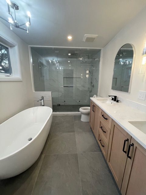 Modern bathroom with a white bathtub, glass shower, and light brown vanity.