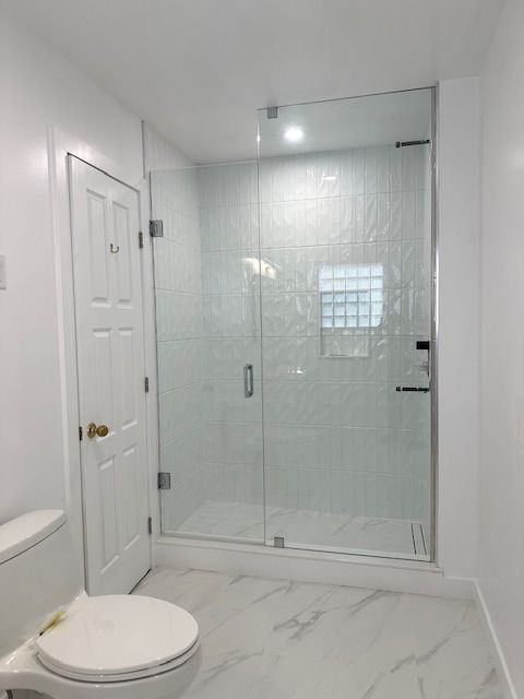 Modern bathroom with white walls, glass shower, toilet, and tile floor.