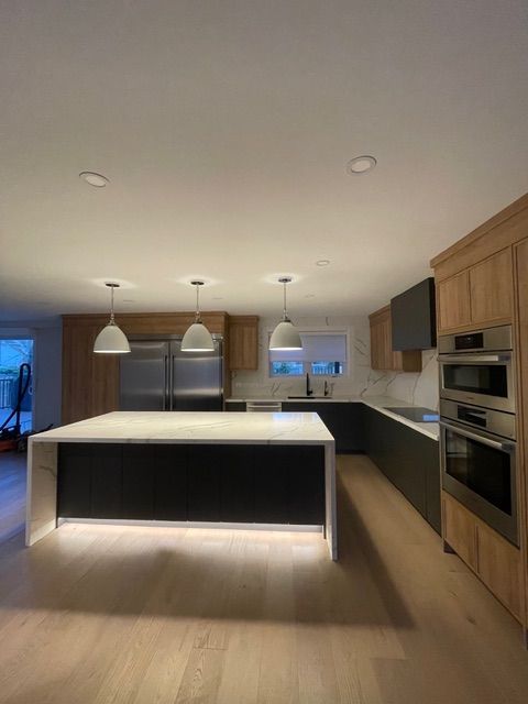 Modern kitchen with island and light wood cabinets, stainless steel appliances, and pendant lights.