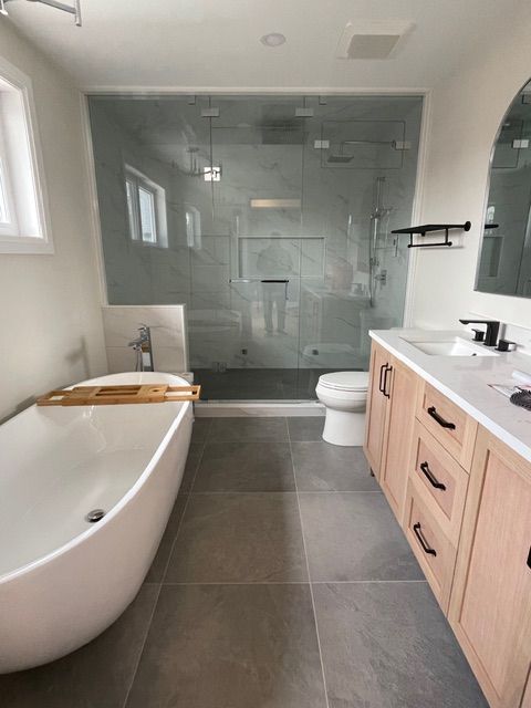 Modern bathroom with a bathtub, glass shower, toilet, vanity, and gray tile floor.