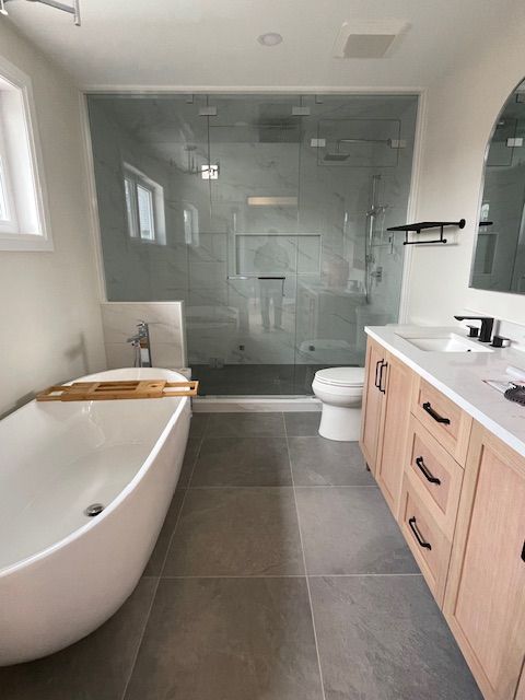 Modern bathroom with freestanding tub, glass shower, light wood vanity, gray tile floor, and white walls.