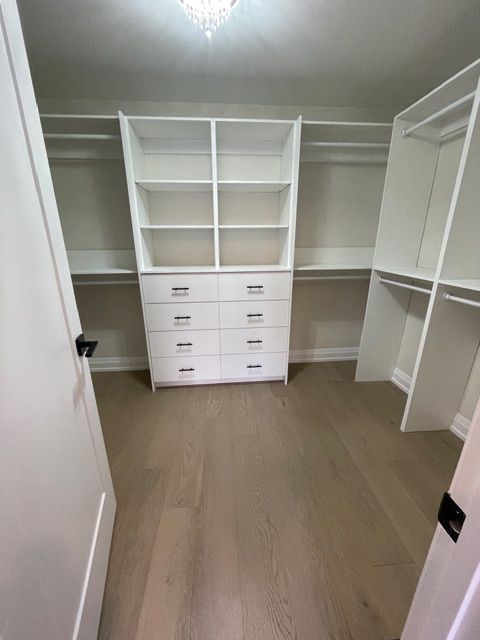 Walk-in closet with white shelves and drawers, wooden floor.