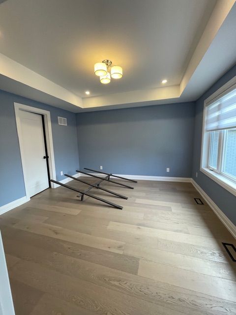 Empty room with blue walls, white trim, and light wood floors. Black metal frames sit on the floor.