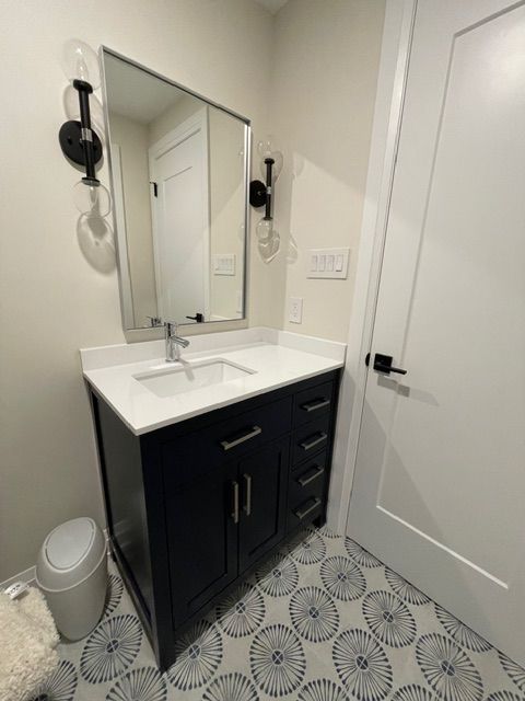 Bathroom with navy blue vanity, white countertop, patterned floor, and black fixtures.