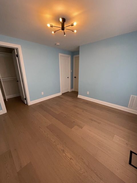 Empty room with light blue walls, wood floor, and white trim. Ceiling light fixture and two white doors.
