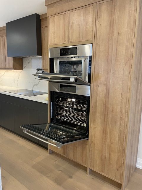 Built-in oven and microwave unit with open doors in a wood-paneled cabinet. Stainless steel appliances in a modern kitchen.