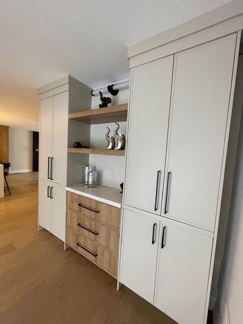 Built-in storage unit with light wood floors. White cabinets, open shelves, and wooden drawers. Black handles.