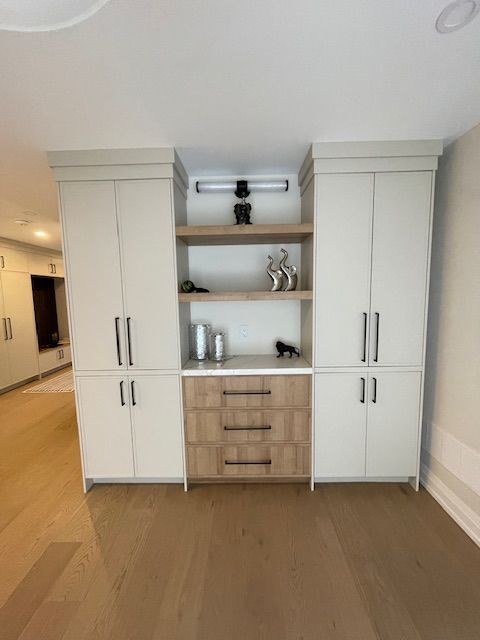 Built-in storage cabinet with light-colored doors, wooden drawers, shelves with decorative items, and wood flooring.