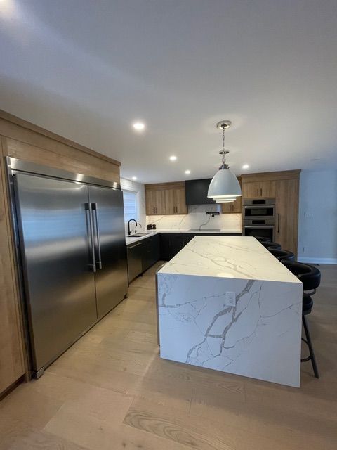 Modern kitchen with light wood cabinets, stainless steel refrigerator, and a white countertop island.