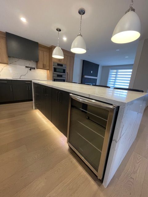 Modern kitchen with island, featuring wine cooler, black cabinets, and pendant lights.
