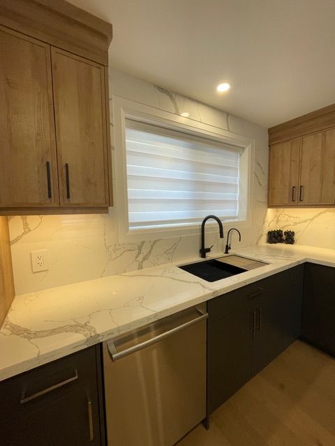 Modern kitchen with wood cabinets, white marble countertops, black sink, and a window with blinds.