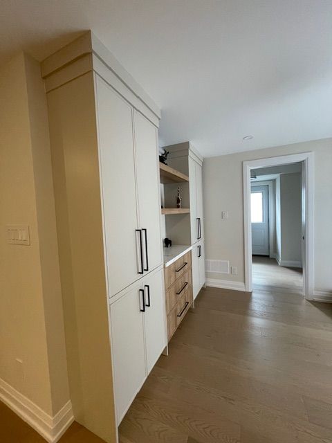 Built-in white storage cabinets with black handles, light wood accents, and shelves against a wall.