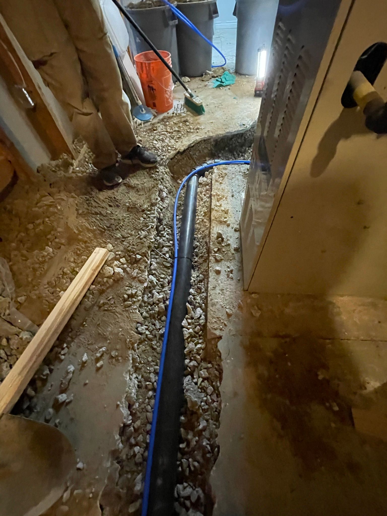 Person in basement trench, laying black pipe and gravel for drainage.