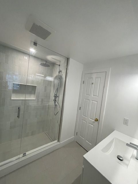 Bathroom with glass shower, white vanity, and closed white door.