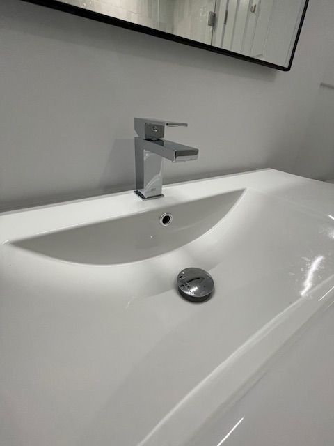 Close-up of a modern white bathroom sink with a chrome faucet and drain stopper, against a white wall.