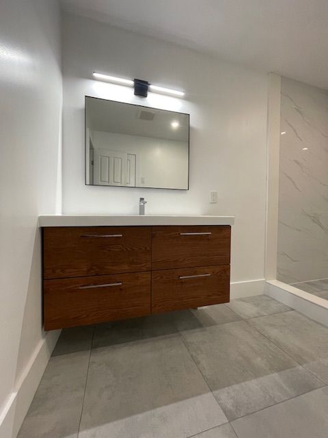 Floating wooden vanity with a mirror, above gray tile flooring in a modern bathroom.