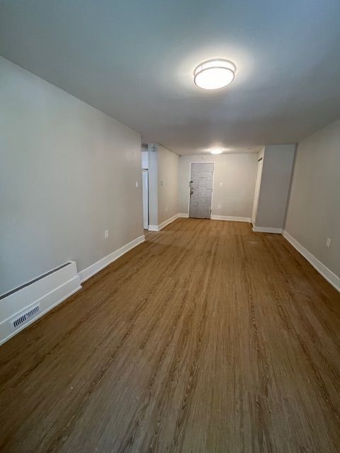 Empty room with wood-look flooring and white walls, door at the back.