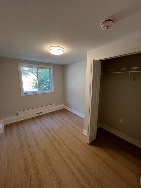 Empty bedroom with wood-look flooring, a closet, window, and a ceiling light. Beige walls.