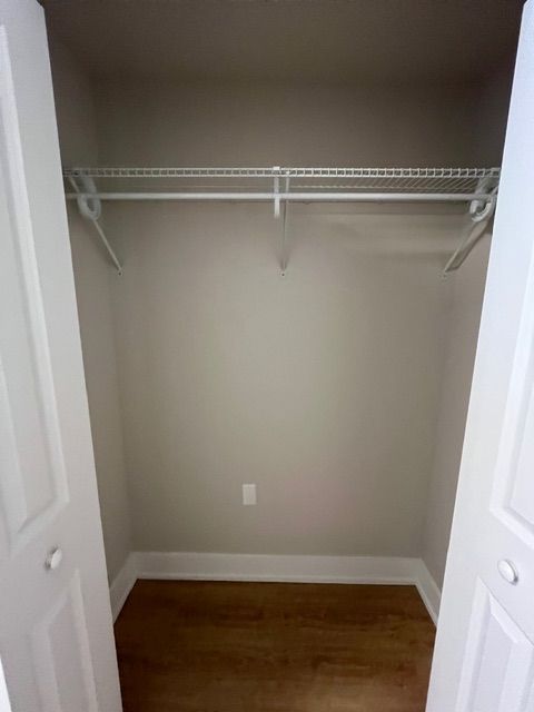 Empty closet with a wire shelf, rod, and hardwood floor. The walls are light gray.