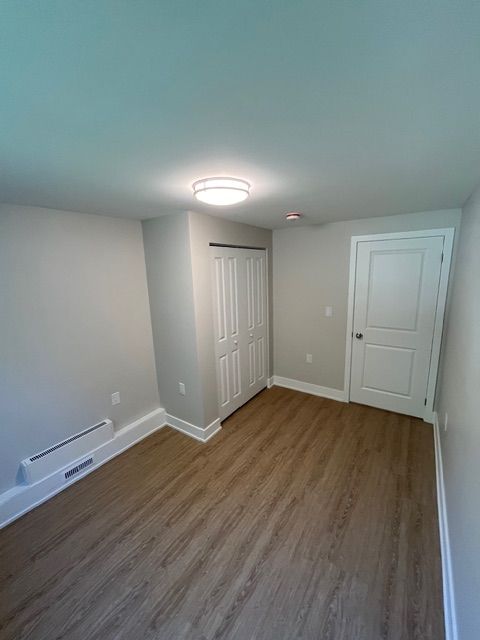 Empty room with light gray walls, white trim, wood-look flooring, a closet, and a closed door.