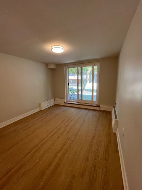 Empty room with wood-look flooring, beige walls, and a sliding glass door.